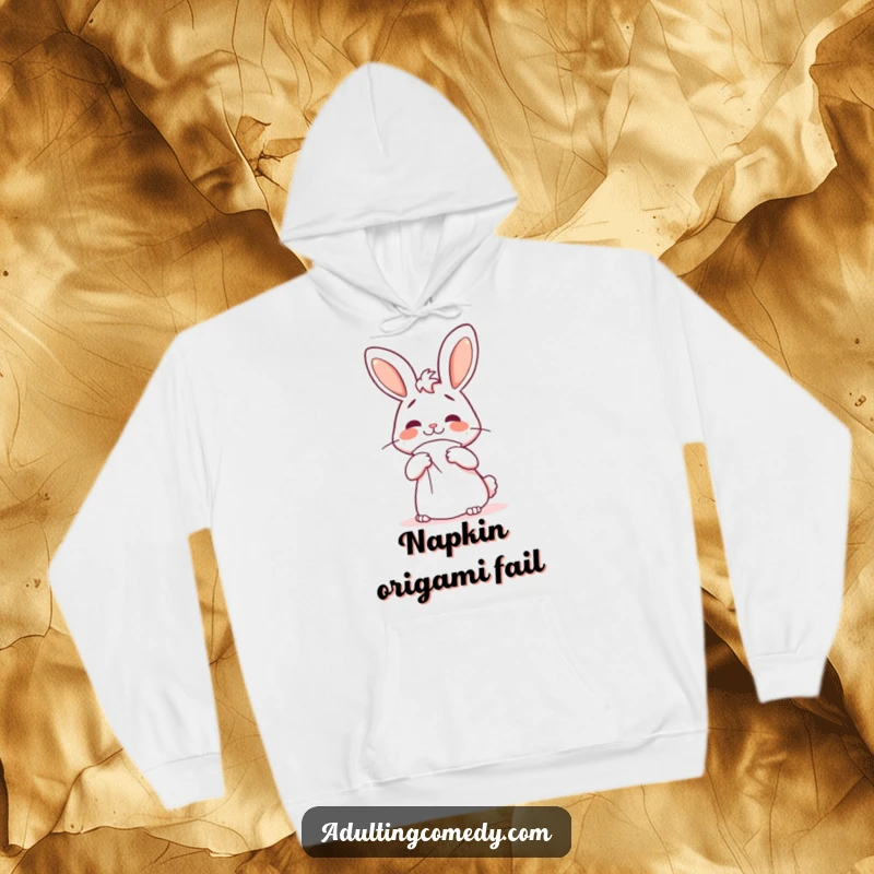 Funny bunny hoodie featuring a cheerful but confused rabbit attempting to fold a giant napkin, a cozy funny gift.